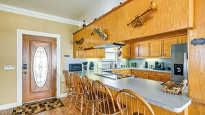 A kitchen with wooden cabinets, a stainless steel refrigerator, and a bar area with wooden chairs.