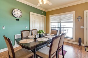 Uma sala de jantar com uma mesa de madeira escura, cadeiras bege, um relógio e uma janela com persianas.