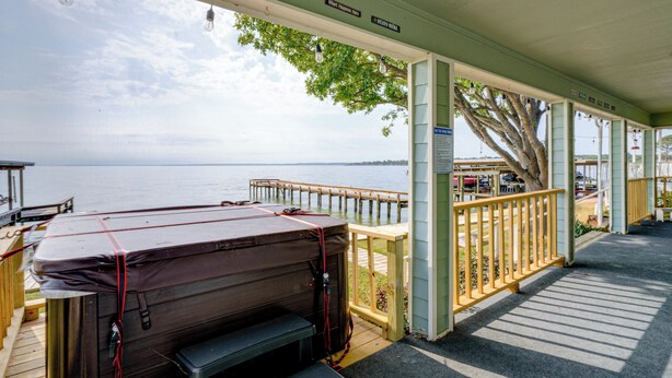 A covered deck with a hot tub, wooden railings, and a view of the water.