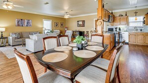 A spacious living room with a large dining table, comfortable seating, and a kitchen area with wooden cabinets and appliances.