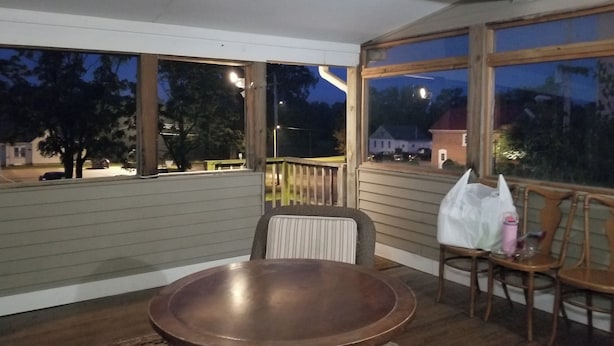 Ein überdachter Außenbereich mit Holztisch und Stühlen, großen Fenstern und Blick ins Freie.