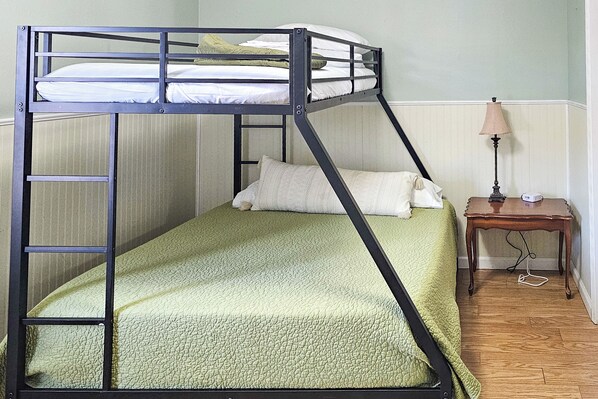 A bunk bed with a green quilt, a wooden nightstand with a lamp, and a white pillow. - Walk to Nauvoo Temple: Remodeled Family Apartment (Nauvoo)