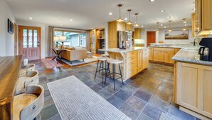 A spacious kitchen with wooden cabinets, a central island, and bar stools. - NW Family Oasis: 6BR Modern Gem Near Rainier! (Puyallup)