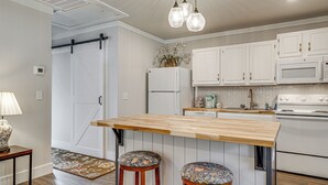 A kitchen with white cabinets, a wooden island, two stools, a refrigerator, a microwave, and a stove. - Wooded Couples Haven! 15 Mi to Wrightsville Beach (Wilmington)