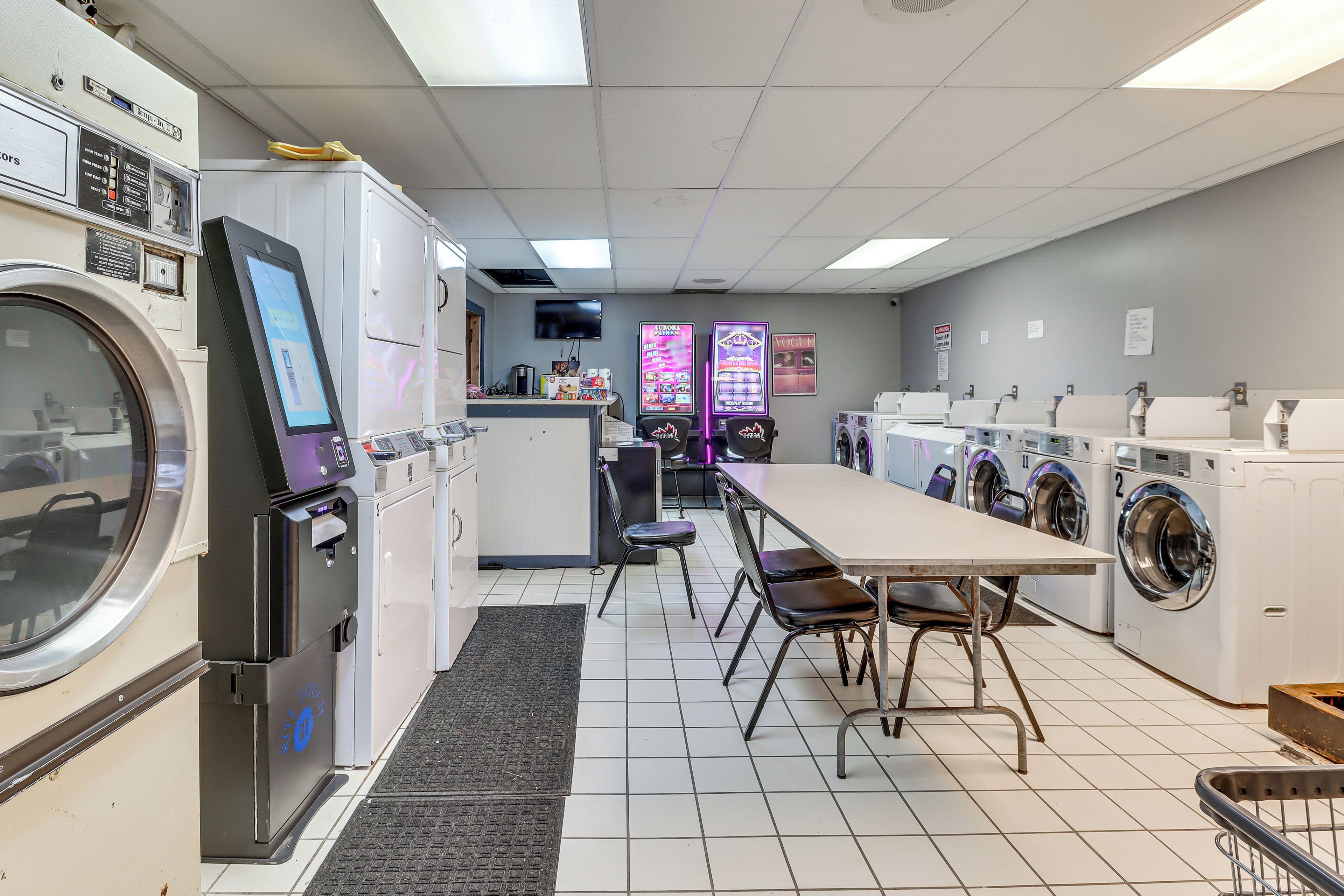 A laundromat with multiple washing machines, a table with chairs, and a vending machine.