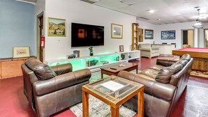 Een woonkamer met leren banken, een salontafel met glazen blad, een flatscreen televisie en een pooltafel.