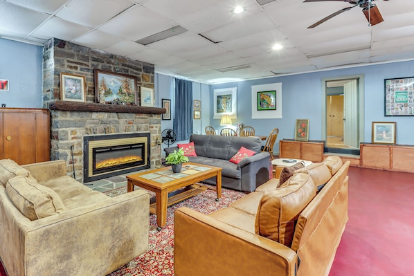 A living room with a stone fireplace, leather sofas, a coffee table, and various framed pictures on the walls. - 4 Mi to Mauch Chunk Lake: Spacious Apt w/ Bar! (Summit Hill)