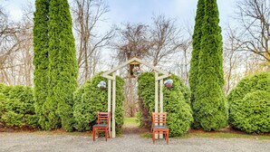 A pathway leading to a wooden archway with two chairs on either side, surrounded by neatly trimmed hedges and tall trees. - 4 Mi to Mauch Chunk Lake: Spacious Apt w/ Bar! (Summit Hill)