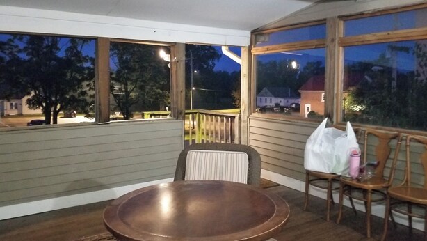 Eine überdachte Veranda mit Holztisch und -stühlen, großen Fenstern und Blick ins Freie.