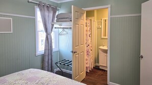 Ein Schlafzimmer mit Bett, Wäscheständer und einem durchgehenden Türrahmen einsehbaren Badezimmer.