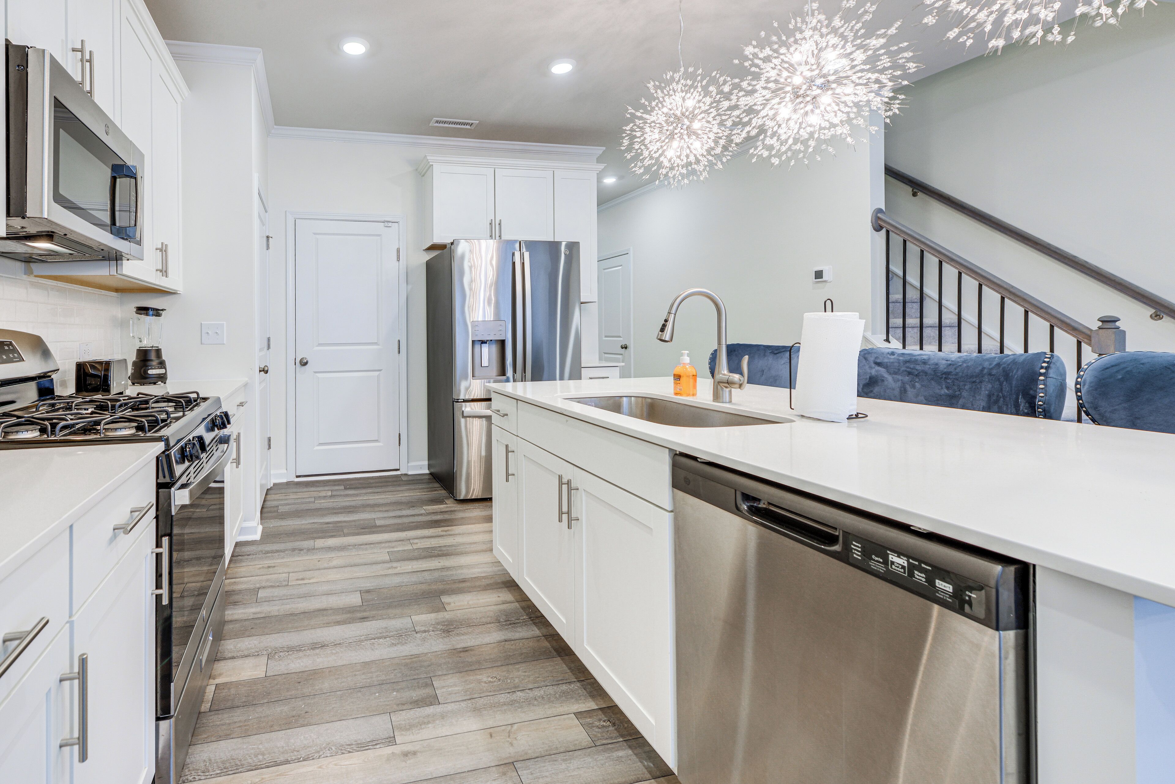 A modern kitchen with stainless steel appliances, white cabinetry, and a wooden floor.
