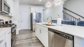 A modern kitchen with stainless steel appliances, white cabinetry, and a wooden floor.