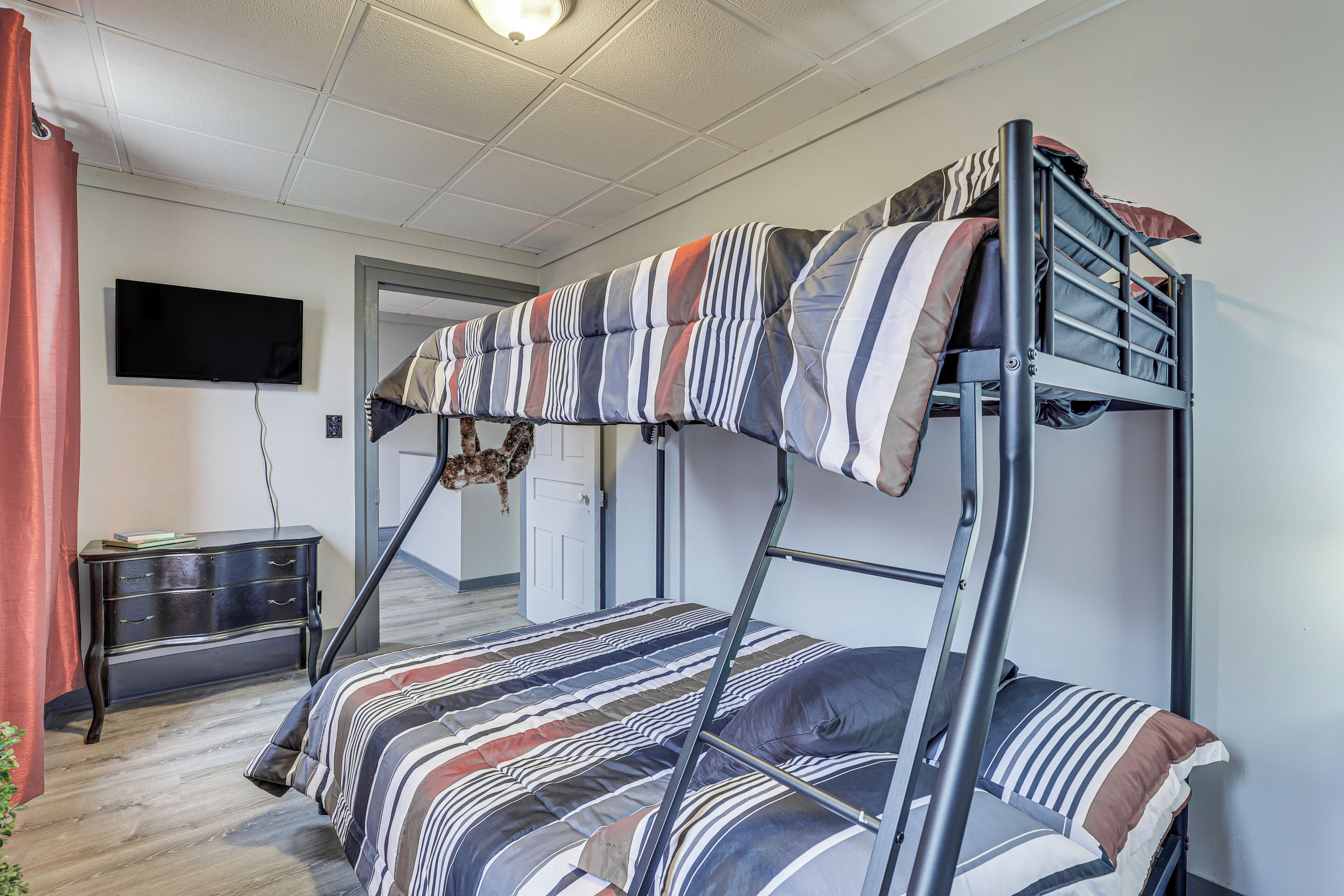 A bunk bed with striped bedding, a flat-screen TV on the wall, a dresser, and a door leading to another room.