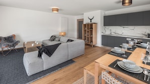 A modern living room with a grey sofa, wooden sideboard, and a dining area with a wooden table set for a meal. - Thélème A201 by Avecoeur (Châtel)