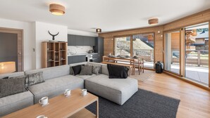 A modern living room with a grey sectional sofa, wooden coffee table, and a kitchen in the background. - Thélème A201 by Avecoeur (Châtel)