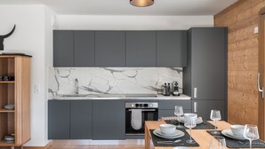 A modern kitchen with grey cabinets, a marble backsplash, and a wooden dining table set for four. - Thélème A201 by Avecoeur (Châtel)
