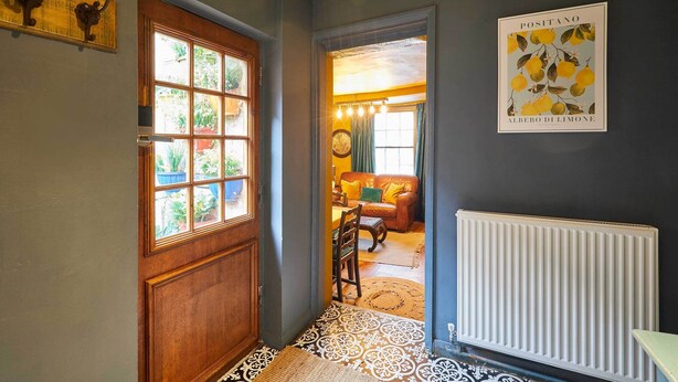 Un corridoio con una porta in legno, un tappeto decorato e un termosifone.