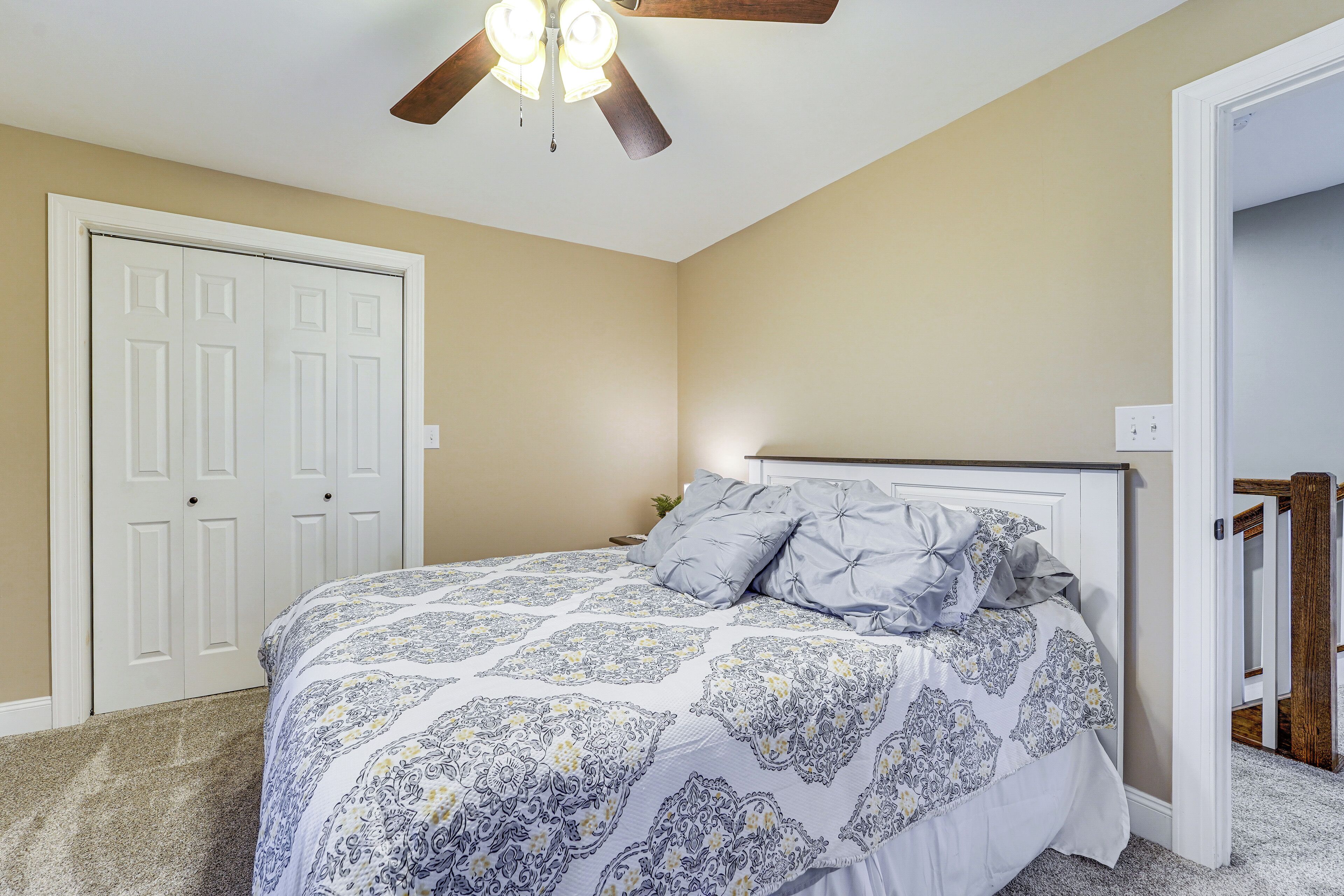 A bedroom with a bed, a ceiling fan, a door, and a staircase.