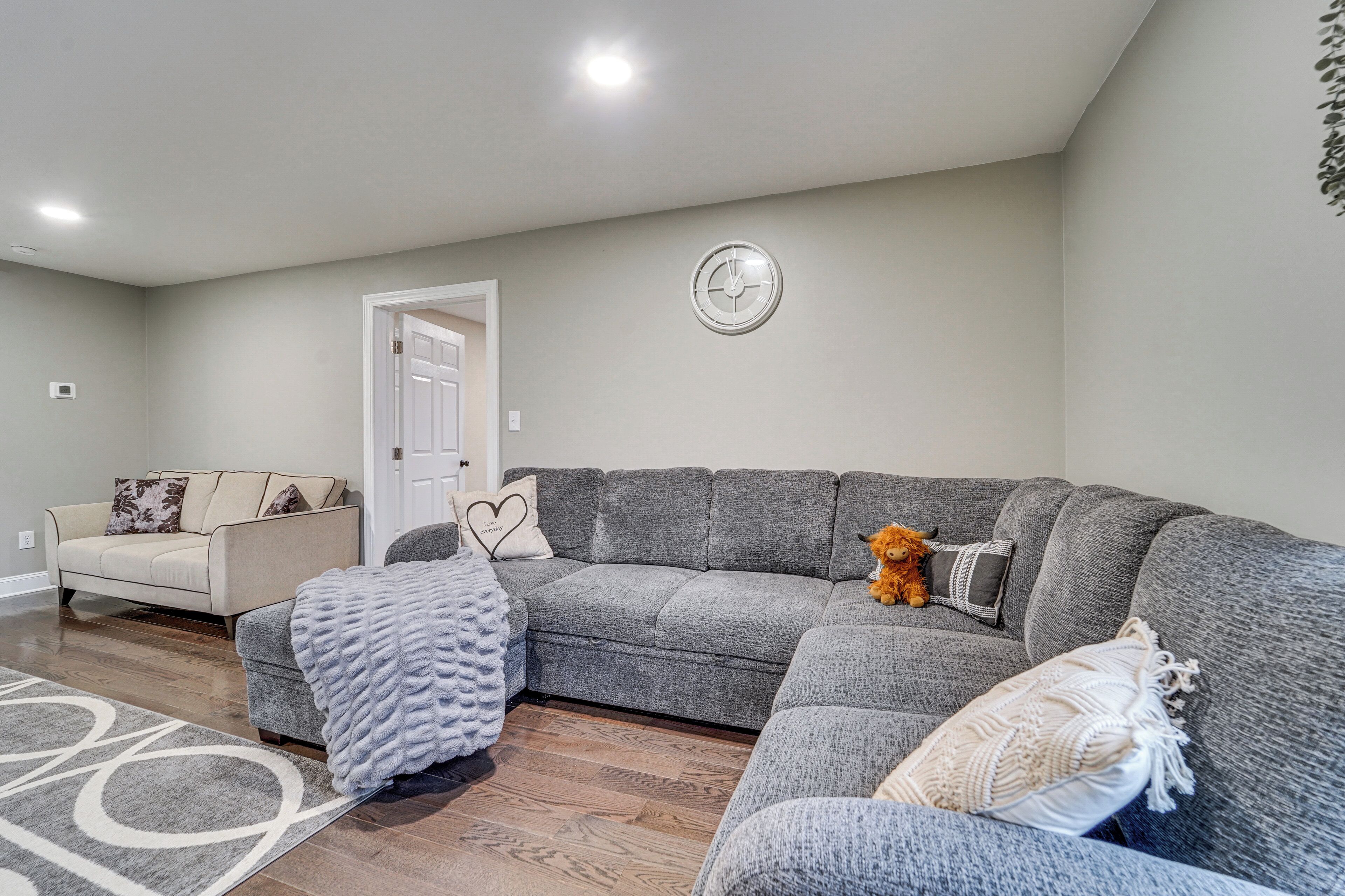Una sala de estar con un sofá seccional gris, un sillón color crema y una puerta blanca.