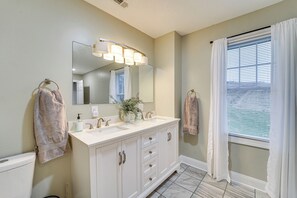 A bathroom with a double sink vanity, a large mirror, and a window with blinds.