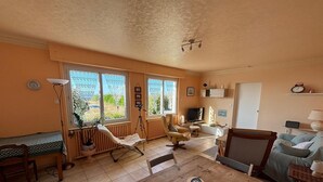 Un ampio soggiorno con un tavolo in legno, posti a sedere confortevoli, una televisione e ampie finestre che si affacciano sull'esterno.