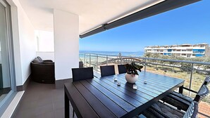 A balcony with a wooden table, chairs, a potted plant, and a view of the sea and buildings. - Dunas Beach II - Sunset Side (Torrox)