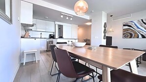A modern kitchen with white cabinets, a coffee machine, and a dining area with a large wooden table and chairs. - Dunas Beach II - Sunset Side (Torrox)