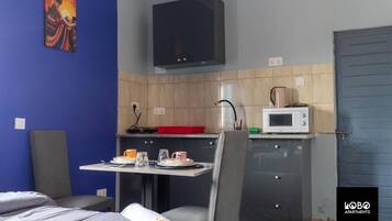 A compact room with a bed, a small dining table with chairs, a kitchenette with a microwave, and a cabinet.