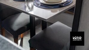 A modern, compact living space with a dining area and a bed. The room features a blue accent wall, a neatly arranged dining table with plates, cups, and a kettle. The bed has a headboard and multiple pillows. - Lobo studio apartments (Serrekunda)