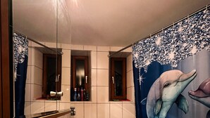 Ein Badezimmer mit einem großen Spiegel, einem Waschbecken, einer Badewanne und einer Wandmalerei mit Delphinen.