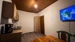 Ein Zimmer mit Holzboden, einem an der Wand montierten Fernseher, einem Holztisch und einer Küchenzeile.