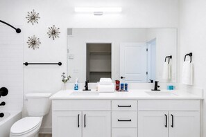 A modern bathroom with a white sink, black faucet, and a mirror above it. There are decorative star-shaped wall decorations and a towel rack with white towels. - Refershing Modern APT in A+Location|WorkerFriendly (Sherman)