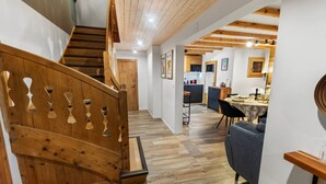 A wooden staircase with a unique design, a dining area with a table and chairs, and a kitchen in the background.