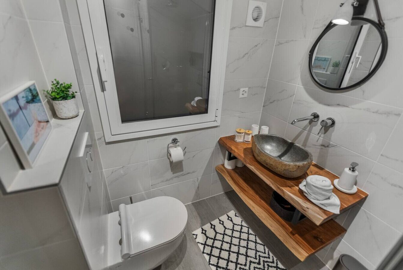 Une salle de bain moderne équipée de toilettes, d’un bidet, d’un meuble-lavabo en bois et d’un grand miroir.
