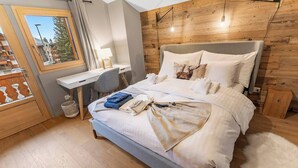 A modern bedroom with a bed, bedside table, desk, and a view through a window.