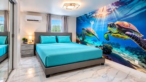 Ein Schlafzimmer mit einem Bett, einem Nachttisch, einem Wandbild von Meeresschildkröten und einem Fenster.