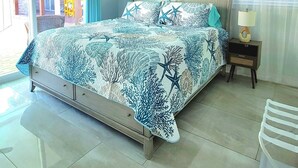 Un dormitorio con cama, ventilador de techo, mesita de noche, lámpara y un cartel que dice 'BEACH'.