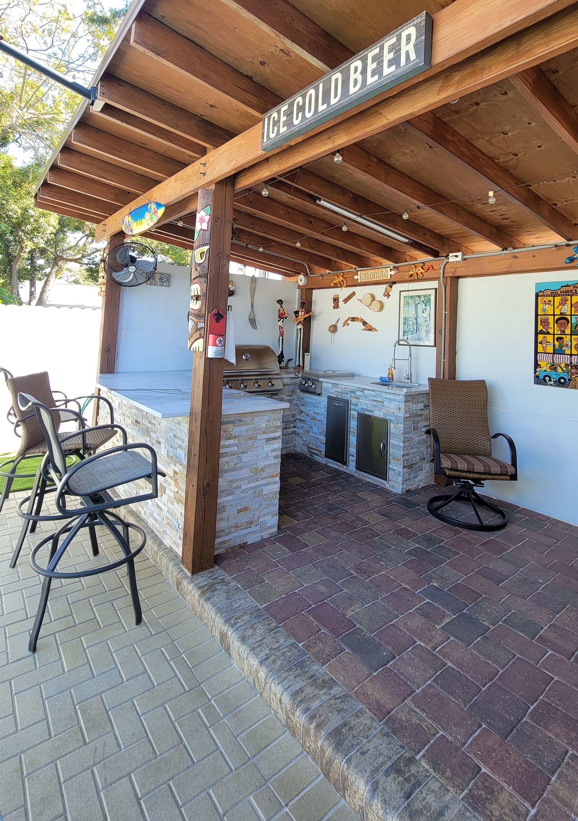 An outdoor bar area with a stone countertop, wooden ceiling, and a sign that reads "ICE COLD BEER".