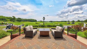 Une terrasse dotée de meubles en osier et offrant une vue sur un terrain de golf.