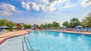 Une piscine à l’eau d’un bleu cristallin, entourée de chaises longues et de parasols, avec une rangée de bâtiments en arrière-plan.