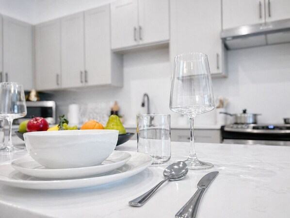 Une cuisine moderne avec des meubles blancs, un plan de travail en marbre, un saladier rempli de fruits et des couverts.
