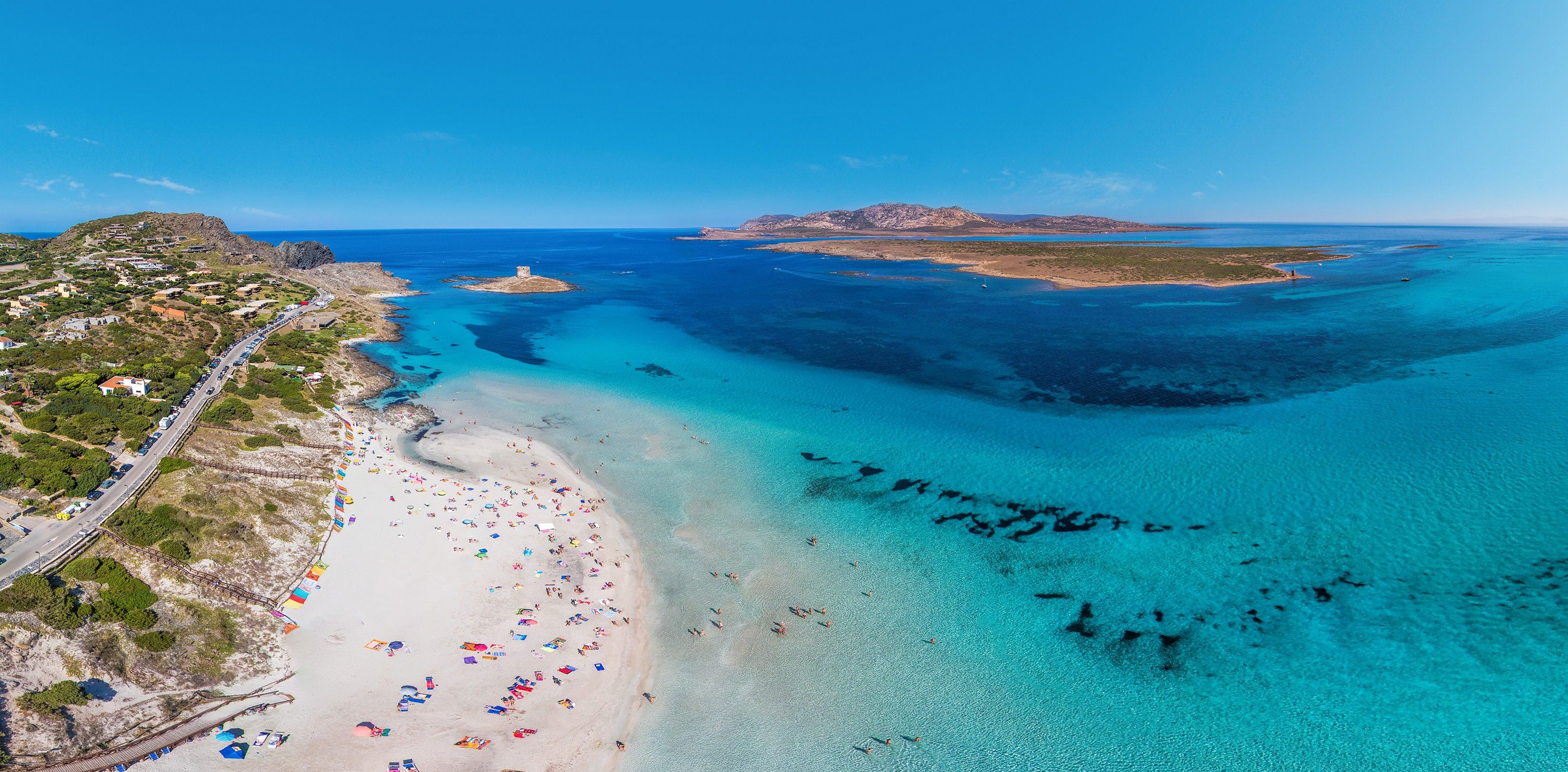 An aerial view of a coastal area with a beach, clear blue waters, and a small island in the distance.