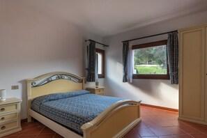 Ein Schlafzimmer mit Bett, Nachttischen, einem Fenster mit Vorhängen und Blick ins Freie.