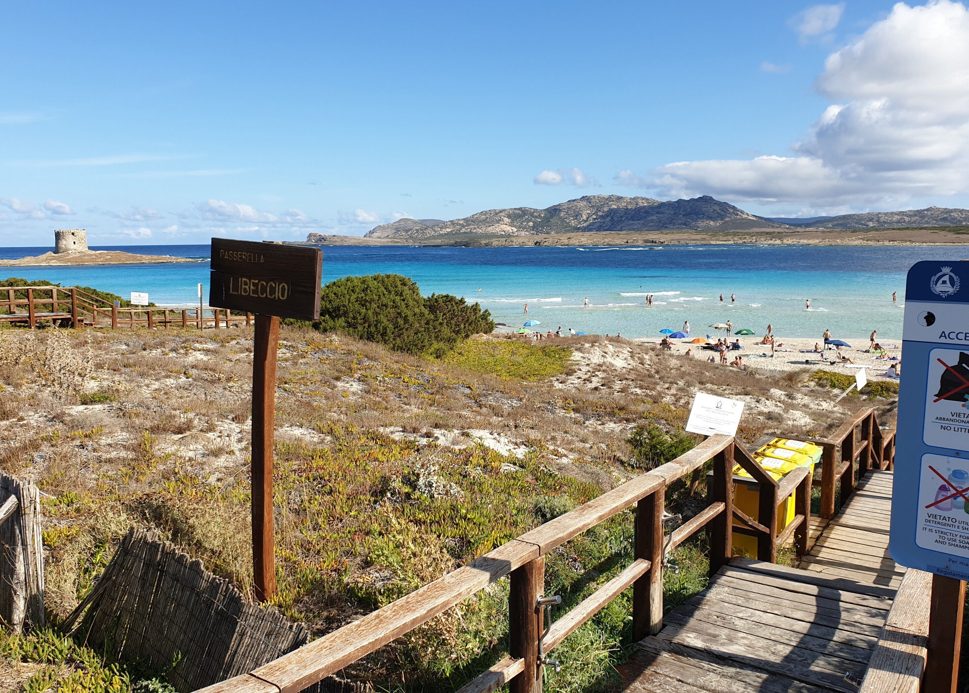 Une plage avec une promenade en bois menant à l’eau, un panneau indiquant « Passefella L’Imbriaccio » et un panneau d’accès à la plage indiquant les interdictions.