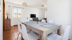 Et spiseområde med et træbord, hvide stole, et fjernsyn og en loftsvift.