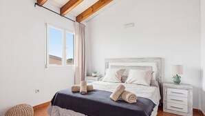 Et soveværelse med en seng, et natbord, en lampe, et vindue og en gardin.