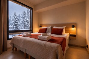 A hotel room with a bed, two bedside tables, a window with a view of snow-covered trees, and a nightstand with a lamp.