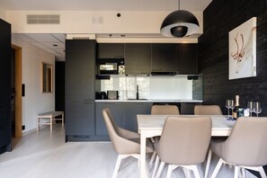 A modern kitchen with dark cabinetry, a dining area with a white table and chairs, and a pendant light above the table.