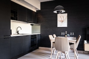 A modern kitchen with dark cabinetry, a white countertop, and a dining area with a table and chairs.