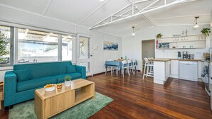 A modern living room with a teal sofa, wooden coffee table, and a dining area with a blue tablecloth. - Love You Moore-Breathtaking Views of Both Ocean and River. (Guilderton)
